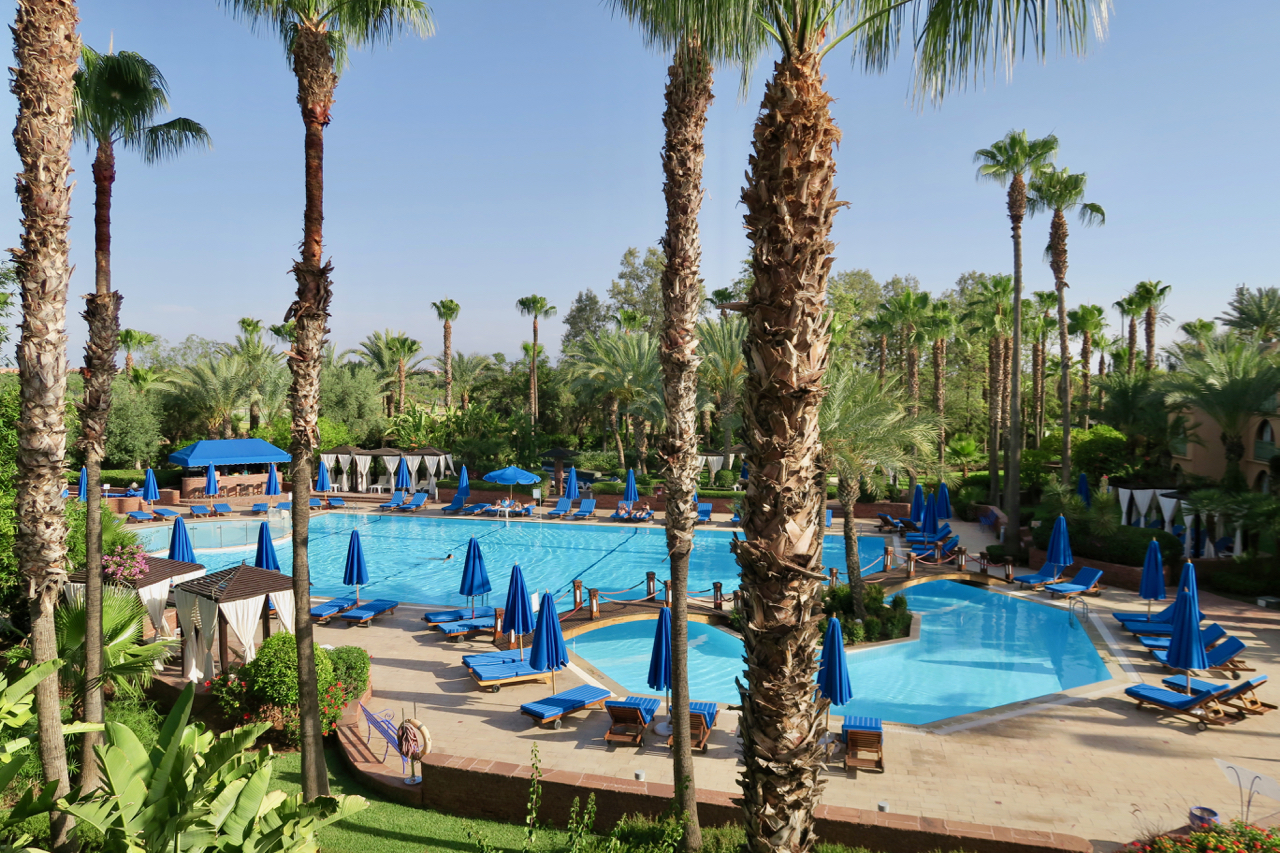 a pool with blue umbrellas and chairs and palm trees