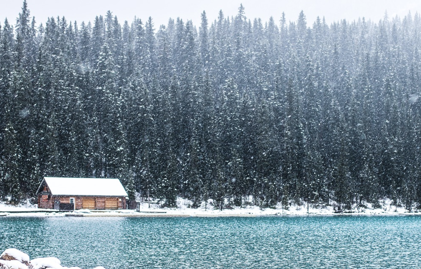 a cabin by a lake with snow falling