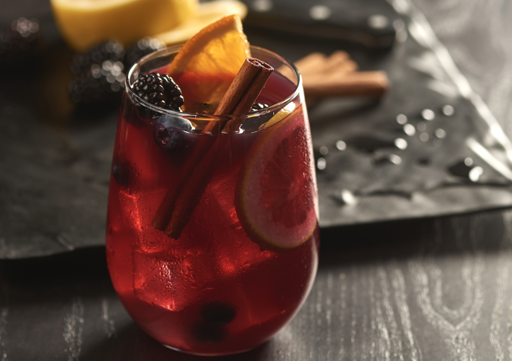 a glass of red drink with fruit and cinnamon sticks